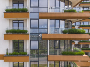 Modernes Mehrfamilienhaus mit großer Fensterfront, braun-weißer Fassade und bepflanzten Balkonen – eine attraktive Immobilie als Altersvorsorge für Menschen, die über den Kauf einer Eigentumswohnung zur privaten Absicherung im Rentenalter nachdenken.