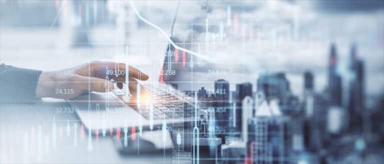 Hand tippt auf Laptop-Tastatur vor urbaner Skyline mit eingeblendeten Börsenkursen und Finanzdiagrammen – symbolisch für die Entscheidung: ETF oder Immobilie als Kapitalanlage.