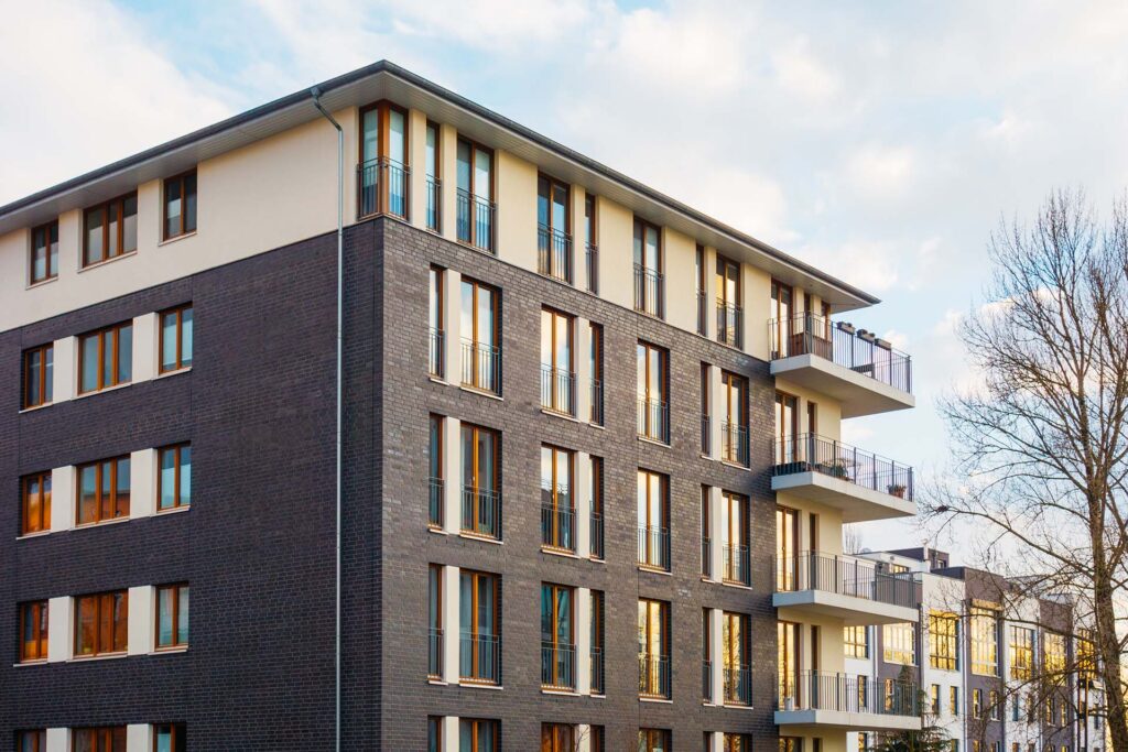 Modern multi-family house with large windows, a dark brick facade, and several balconies.
