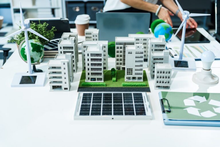 Architekturmodell einer nachhaltigen Stadt mit Miniaturgebäuden, Windkraftanlagen, einem Solarpanel und einem Recycling-Symbol auf einem Schreibtisch.